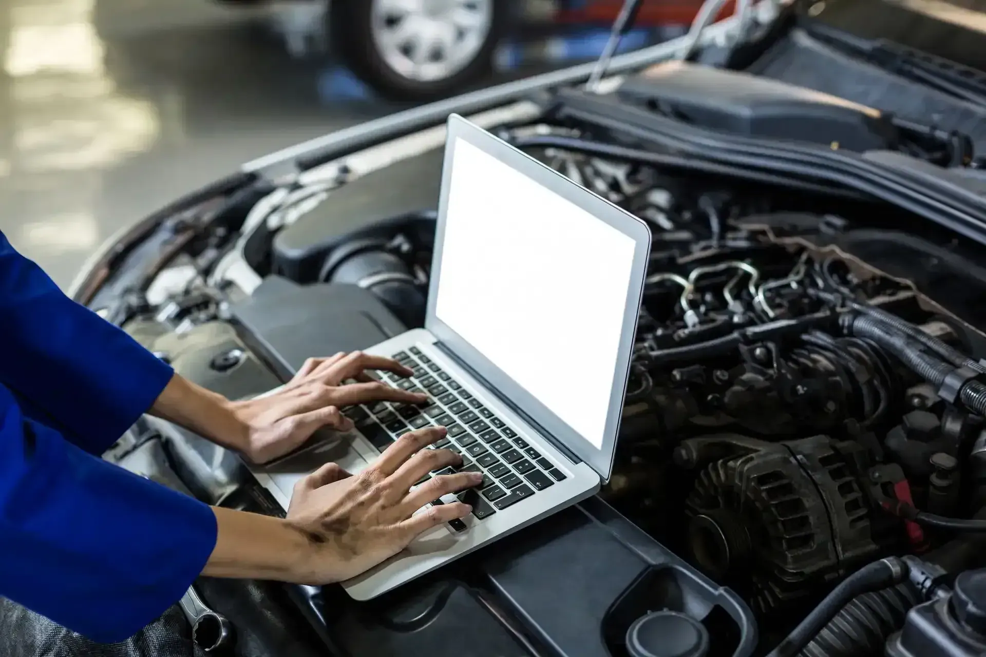 Technician typing on a laptop resting on a car engine during computer diagnostics