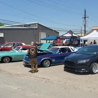 A man is standing in front of a row of cars at a car show.