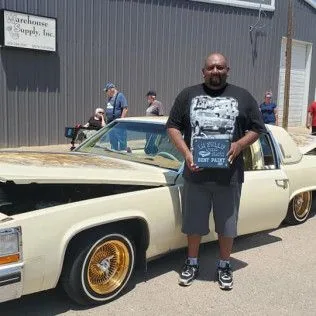 A man is standing in front of a car holding a plaque.
