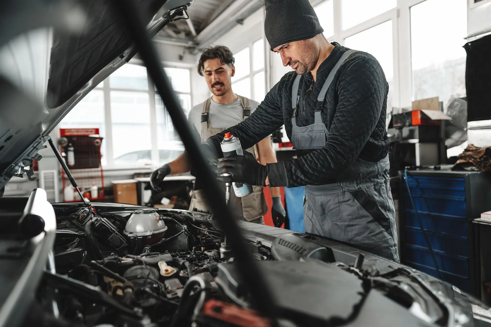 Two mechanics adding fluid under the hood of a car during routine maintenance
