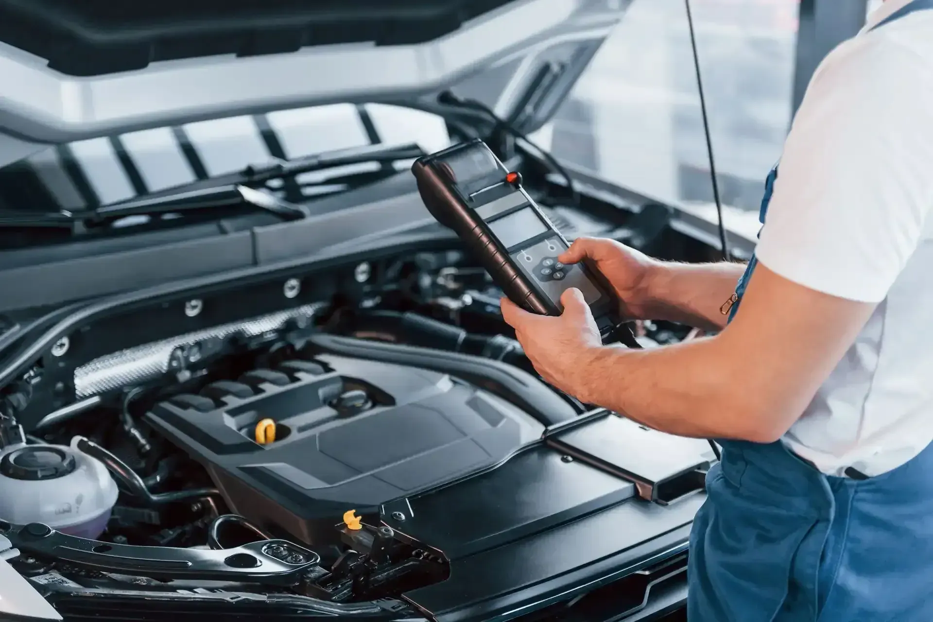 Technician reading a handheld diagnostic scanner over an open car engine
